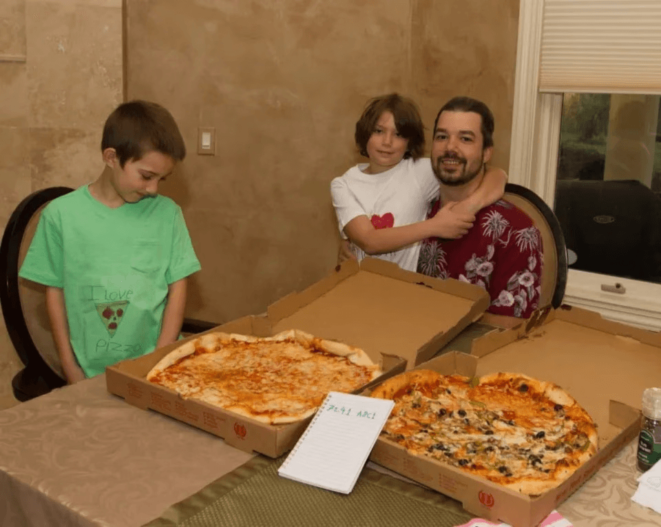 A photo of people gathered around a table sharing two pizzas.